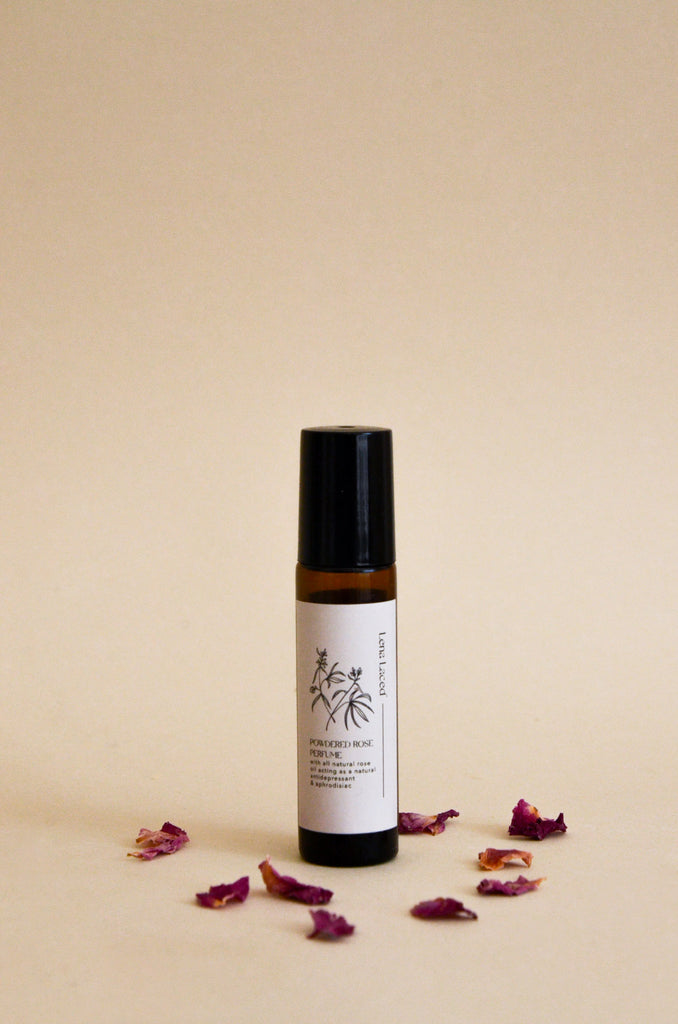 a small brown glass roll on rose perfume surrounded by rose petals. 