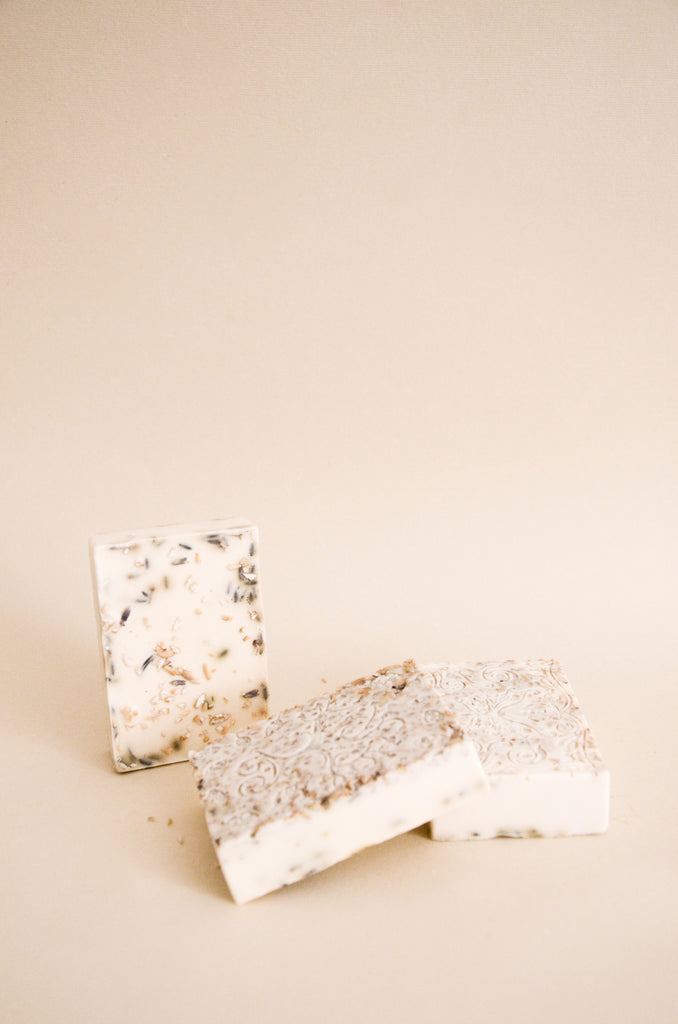 3 Oatmeal lavender soapbars, one.standing up in the back and the two on the right are slightly stacked. The bars have a tree and a butterfly stamped on the top. 